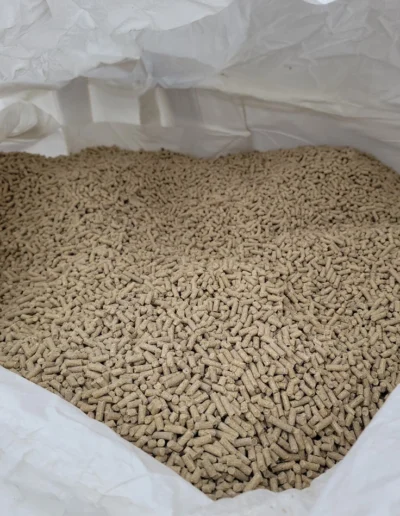 A close-up image of densely packed light brown pellets, used for animal feed, stored in a tote bag